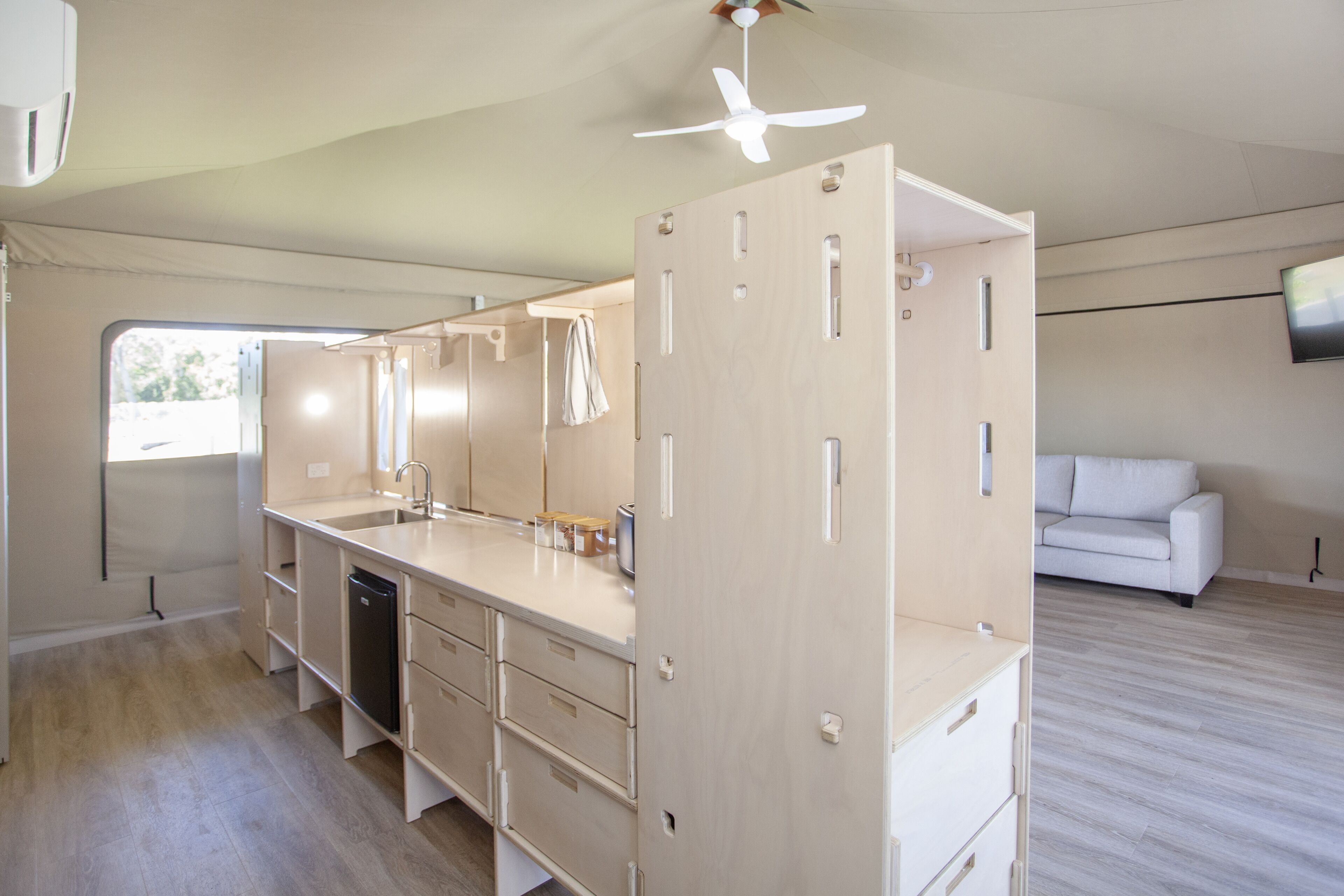 A compact kitchen with a dishwasher, a sink, and a ceiling fan. There is a white sofa in the adjacent living area.