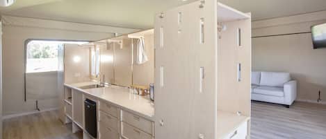 A compact kitchen with a dishwasher, a sink, and a ceiling fan. There is a white sofa in the adjacent living area.
