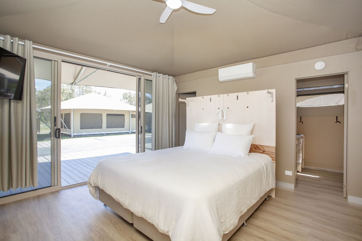 A bedroom with a large bed, sliding glass doors to a balcony, a ceiling fan, and a built-in wardrobe.