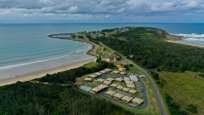 Vista aérea de un complejo turístico costero con propiedades frente a la playa, una piscina y un camino que conduce a la playa.