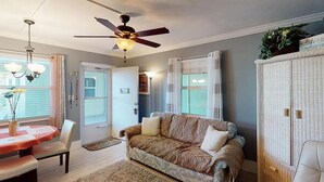 A cozy living room with a ceiling fan, a dining table with chairs, a patterned sofa, and a wicker cabinet. -  Charming Condo in Marco Island (Marco Island)