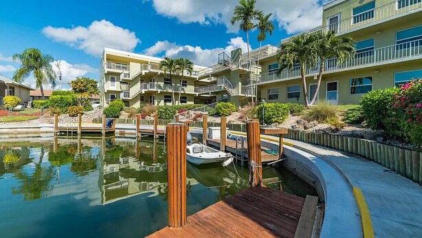 A marina with a dock, a boat, and a multi-story building with balconies. -  Charming Condo in Marco Island (Marco Island)