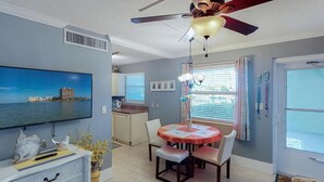 A living room with a ceiling fan, a flat-screen TV, a dining table with chairs, and a kitchen area in the background. -  Charming Condo in Marco Island (Marco Island)