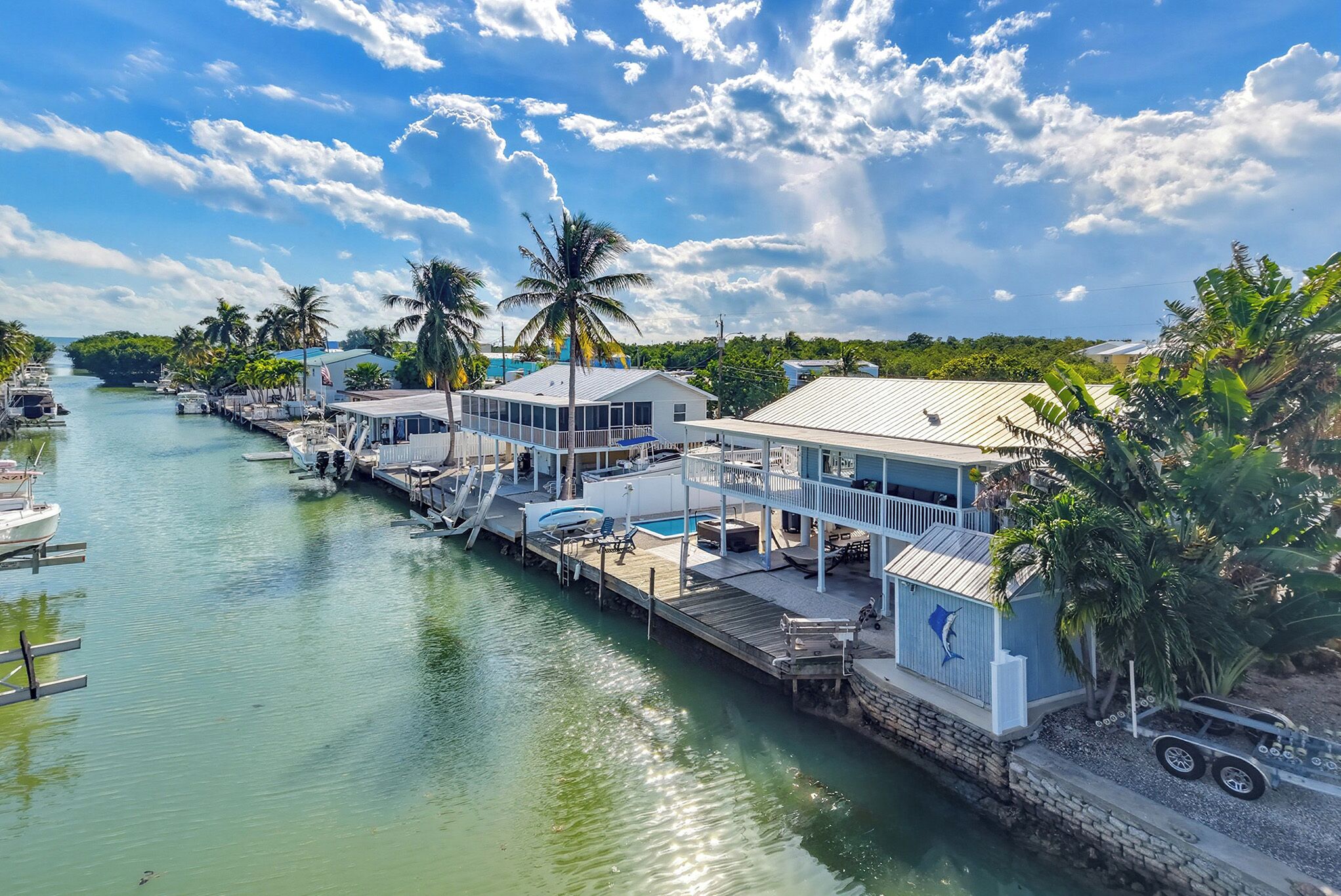 A waterfront property with docked boats, a swimming pool, and a dock extending into the water.