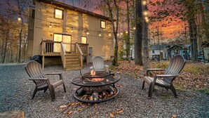 Eine Holzhütte mit Feuerstelle und zwei Adirondack-Stühlen davor.