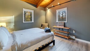 Ein Schlafzimmer mit einem Bett, einem Sessel, einer Bank und zwei Fenstern mit gerahmten Bildern.