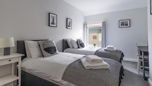 Ein modernes Schlafzimmer mit zwei Betten, einem Schreibtisch und einem Fenster mit Vorhängen.