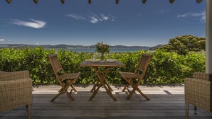 A wooden deck with a table and chairs, overlooking a scenic view of the sea and hills.