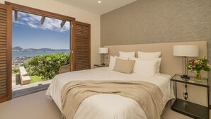 A bedroom with a large bed, two bedside tables with lamps, a view of the outdoors, and a patterned wall.