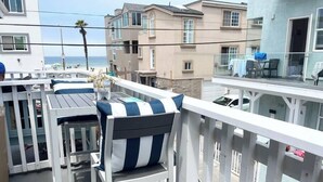 Un balcon avec une balustrade blanche, une table avec des chaises et une vue sur la plage et l’océan.