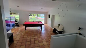 A room with a pool table, a sofa, and a view of a backyard with a pool. - KING BED SUITE w. Large Backyard, 2 LVRMs & 2 FLs (Lauderhill)