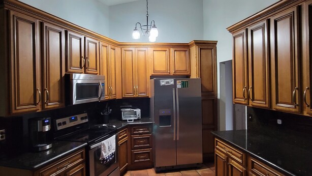 A kitchen with wooden cabinets, stainless steel appliances, a black countertop, and a tiled floor. - KING BED SUITE w. Large Backyard, 2 LVRMs & 2 FLs (Lauderhill)