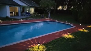 A swimming pool with a red border, surrounded by a garden with small lights. - KING BED SUITE w. Large Backyard, 2 LVRMs & 2 FLs (Lauderhill)