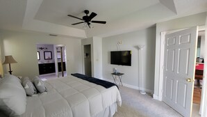 A bedroom with a bed, ceiling fan, TV, and a door leading to another room. - KING BED SUITE w. Large Backyard, 2 LVRMs & 2 FLs (Lauderhill)