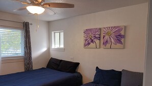 Ein Schlafzimmer mit zwei Betten, einem Deckenventilator, einem Fenster mit Jalousien und zwei an der Wand befestigten Blumenbildern.