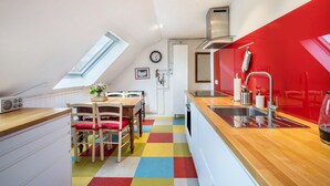 Een keuken met een rode accentmuur, een houten eettafel met stoelen, een kleurrijke geruit vloer en een dakraam.