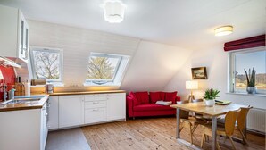 Una cocina moderna con sofá rojo, mesa de comedor y sillas, una ventana pequeña y un radiador.