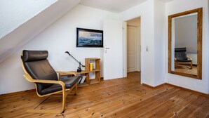 Una habitación con techo inclinado, un sillón de cuero negro, un escritorio de madera, una estantería y un cuadro en la pared.