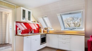 Una cocina moderna con armarios blancos, una pared de acento roja, un tragaluz y vistas a árboles.
