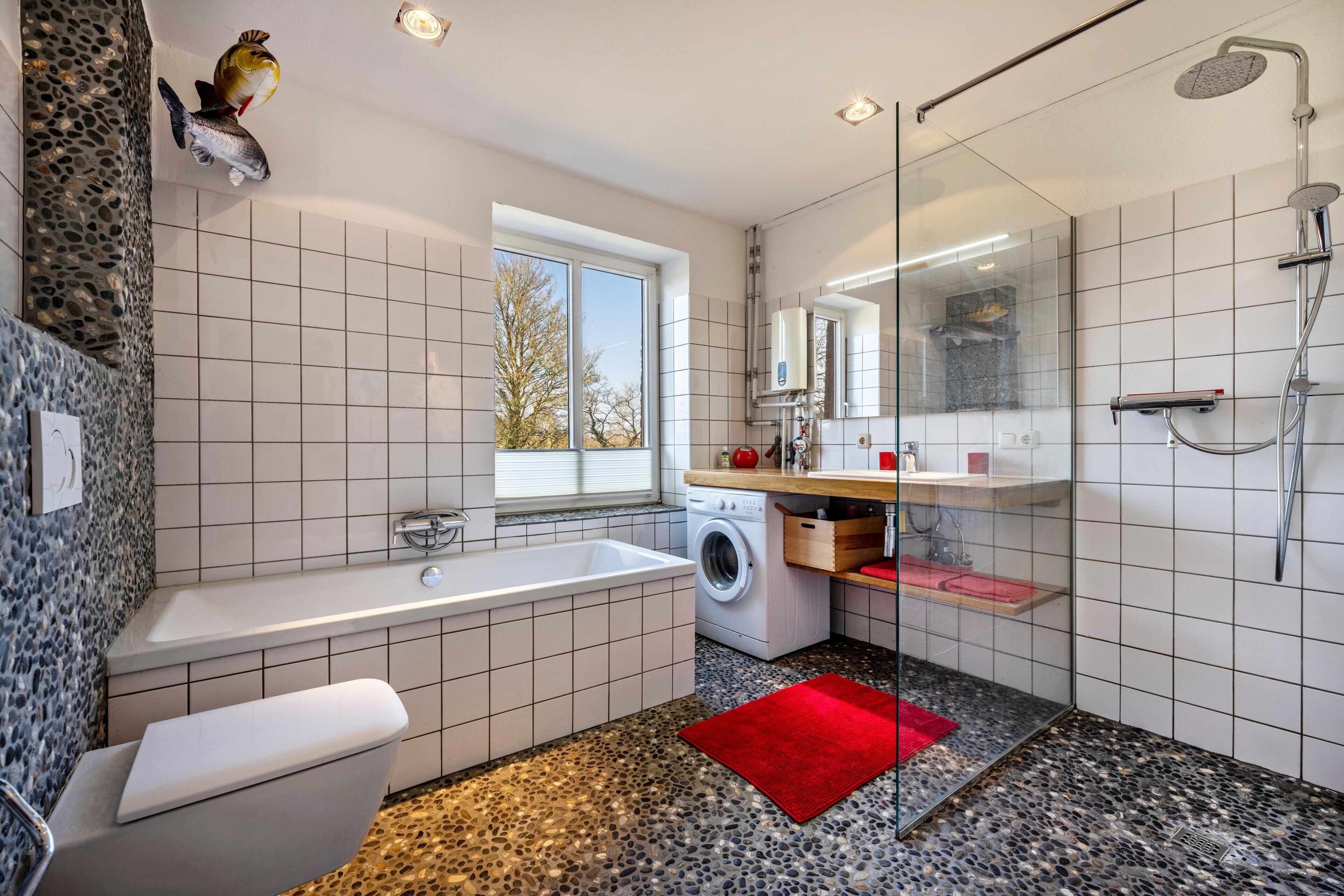 Ein modernes Badezimmer mit Badewanne, Waschmaschine, Duschkabine aus Glas und einem roten Teppich.