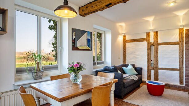 A dining area with a wooden table and chairs, a sofa, and a red ottoman. - Apartment "Voßberg Ferienwohnung 1" with Shared Terrace & Wi-Fi (Grömitz)