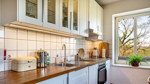A modern kitchen with white cabinets, a stainless steel sink, and a window with a view of trees. - Apartment "Voßberg Ferienwohnung 1" with Shared Terrace & Wi-Fi (Grömitz)