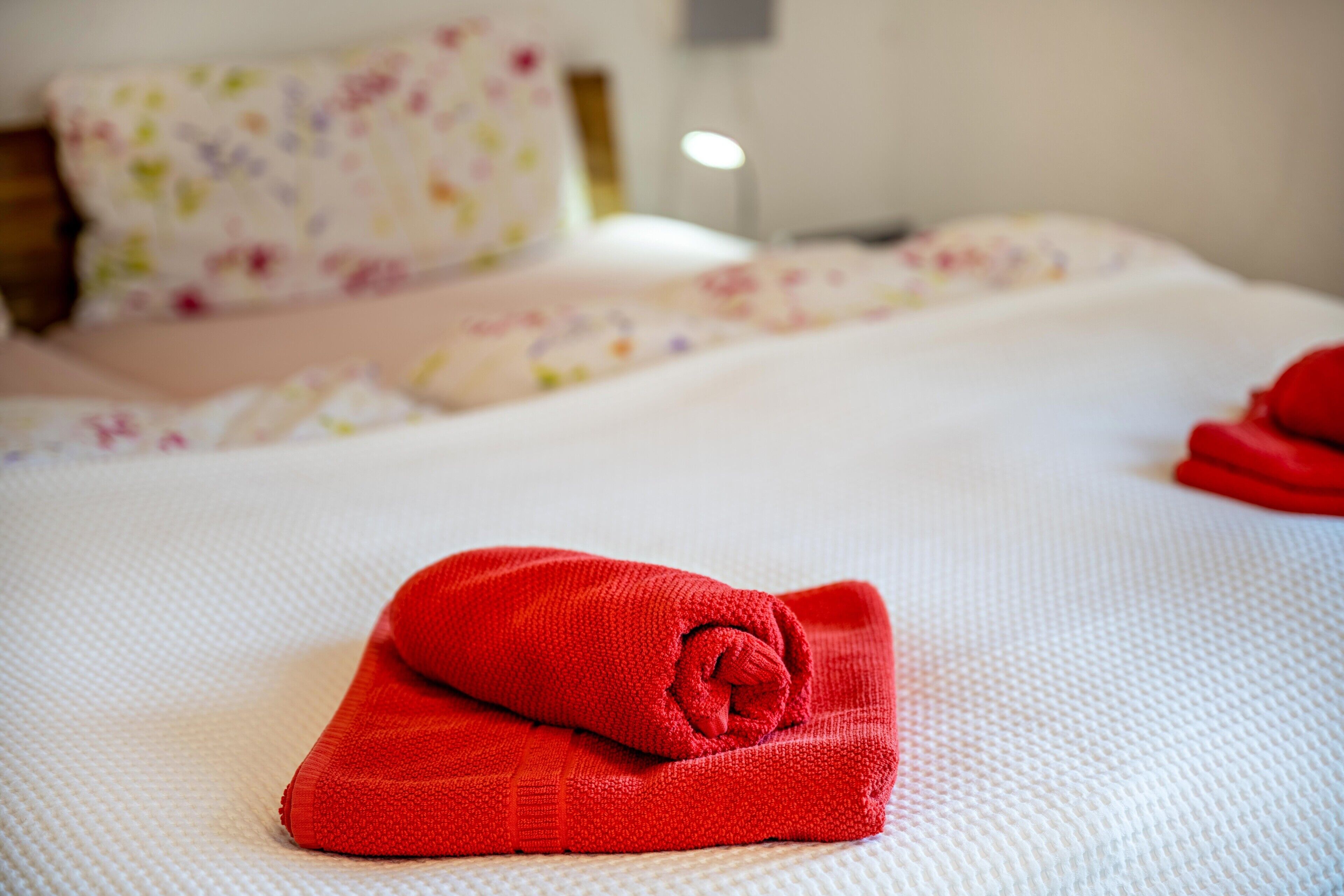 Un lit bien fait, avec une serviette rouge, un coussin à motifs floraux et un couvre-lit blanc.