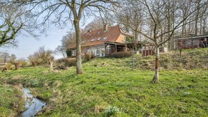 A house with a sloped roof, a small stream, and a grassy area with trees. - Apartment "Voßberg Ferienwohnung 1" with Shared Terrace & Wi-Fi (Grömitz)