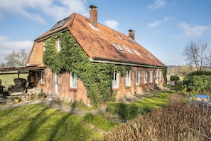 Une maison en briques avec un toit en pente, des murs recouverts de lierre et un porche avant visible, agrémenté d’un banc.