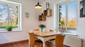 A dining area with a wooden table, chairs, a vase with flowers, a clock, and shelves with books and a plant. - Apartment "Voßberg Großes Ferienhaus" with Shared Terrace & Wi-Fi (Grömitz)