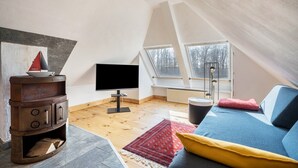 A loft bedroom with a television, wooden flooring, a red patterned rug, a sofa with yellow cushions, and a rustic wooden cabinet. - Apartment "Voßberg Großes Ferienhaus" with Shared Terrace & Wi-Fi (Grömitz)