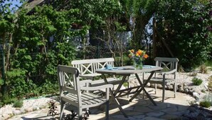 An outdoor patio with a stone table and white wooden chairs, surrounded by greenery and a stone pathway. - Apartment 'Ullo´s Schwalbennest  ' with Private Terrace, Shared Garden and Wi-Fi (Lütow)