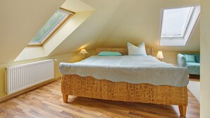 A bedroom with a sloped ceiling, a bed with a woven headboard, two bedside lamps, and a window. - Apartment 'Ullo´s Schwalbennest  ' with Private Terrace, Shared Garden and Wi-Fi (Lütow)
