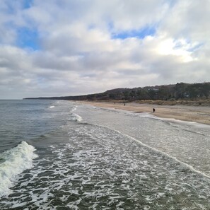 A beach with waves, a distant shoreline, and a cloudy sky.