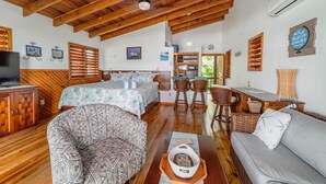 Una habitación acogedora con una cama, un sofá, un sillón estampado, una zona de comedor con sillas de mimbre y una pequeña cocina.