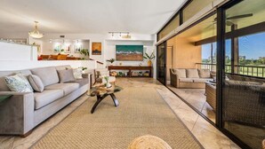 A spacious living area with a sofa, coffee table, and a dining area with a view of the outdoors.