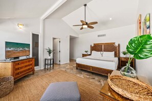 A bedroom with a bed, a television, a ceiling fan, a large plant, and a wooden dresser.