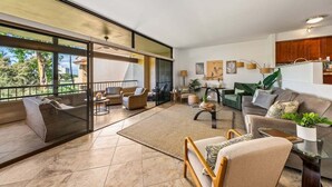A spacious living area with a large sliding glass door leading to a balcony, furnished with a sofa, chairs, and a coffee table.