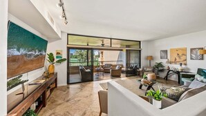 A spacious living area with a large TV, comfortable seating, and a balcony with a view.