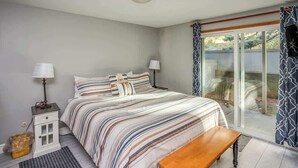 A bedroom with a bed, bedside tables, a bench, and a view through a sliding glass door.