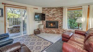 A living room with a fireplace, leather sofas, a TV, and a glass door leading to an outdoor area.