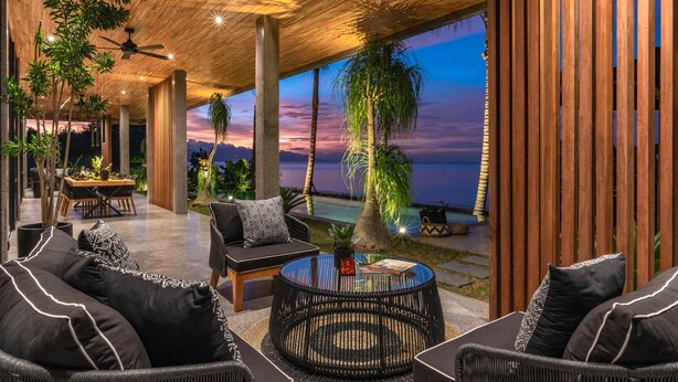 Un espace intérieur moderne comprenant un coin repas, des sièges et une vue sur l’océan au coucher du soleil.