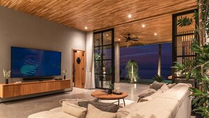 Un salon moderne doté d’un grand téléviseur, d’un plafond en bois et offrant une vue sur l’océan.