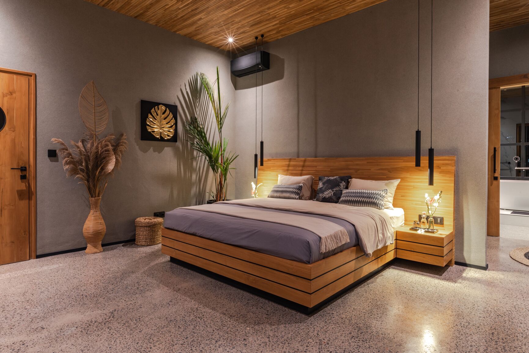 A modern bedroom with a wooden bed, a nightstand, a wall-mounted air conditioner, and a large plant.