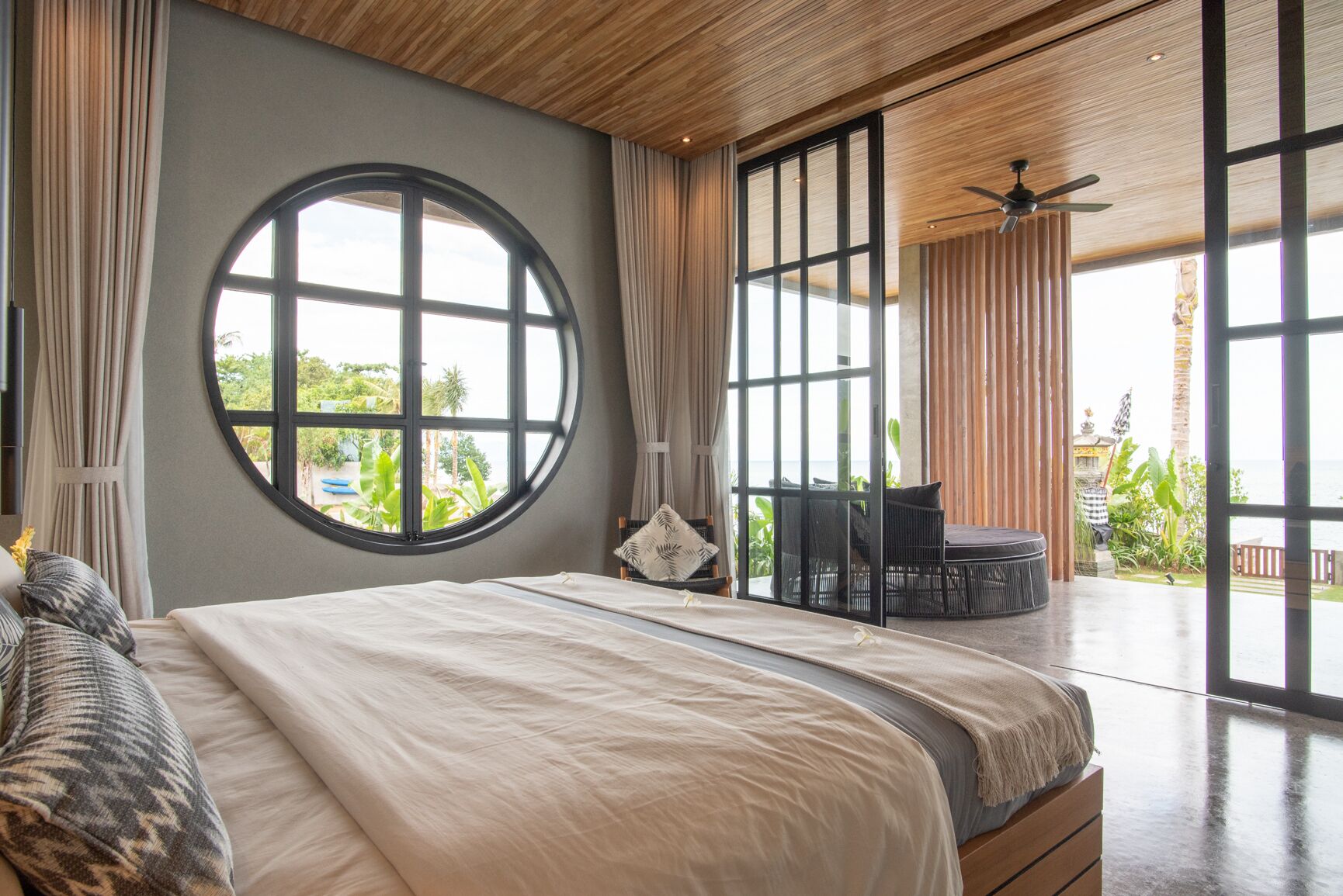 Un dormitorio con un ventanal grande y redondo, una cama, un ventilador de techo y vistas al exterior.