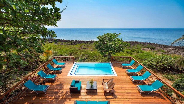 A wooden deck with a pool, lounge chairs, and a view of the ocean.