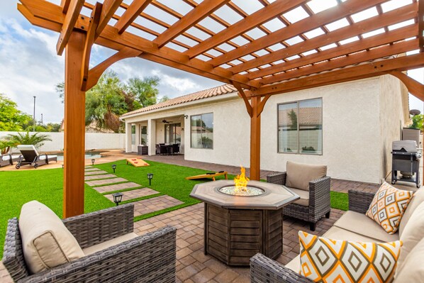 Un patio con mobiliario exterior, una fogata y una pérgola.