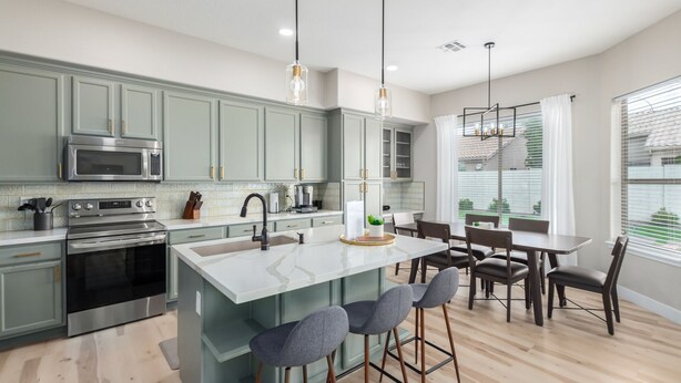 A modern kitchen with a central island, bar stools, and a dining area with a large window. - Edgemont Escape-  3 King Beds, heated pool*, close to spring training,  (Goodyear)