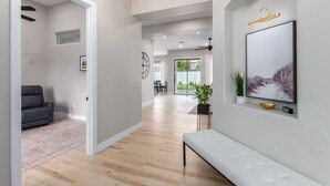 A spacious hallway with a bench, a dining area, and a large window offering a view of the outdoors. - Edgemont Escape-  3 King Beds, heated pool*, close to spring training,  (Goodyear)