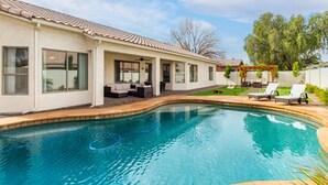 A swimming pool with a tiled deck, a covered patio area with seating, and a pergola with outdoor furniture. - Edgemont Escape-  3 King Beds, heated pool*, close to spring training,  (Goodyear)
